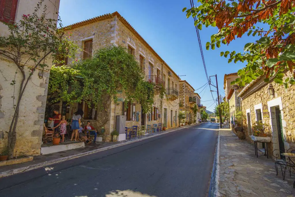 Charming stone street in Kardamili, Greece with traditional buildings, vine-covered cafés, and outdoor seating.