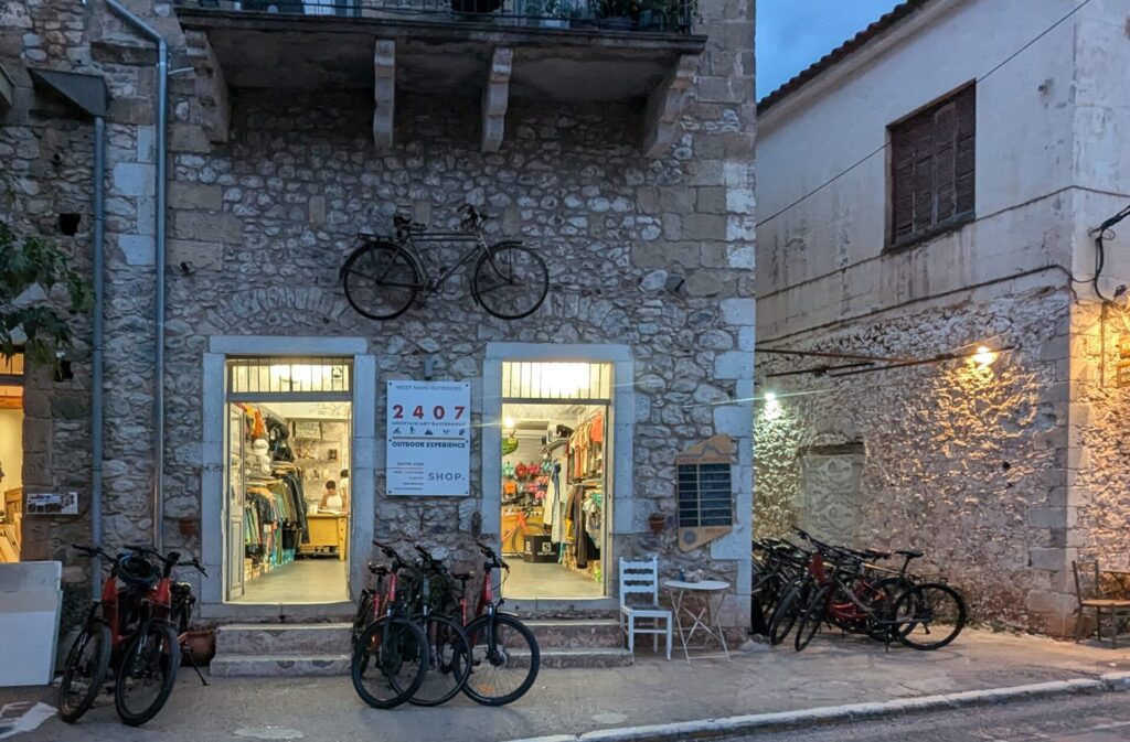 The entrance of the 2407M Outdoor Experience shop in Kardamili, showcasing bikes and adventure gear.