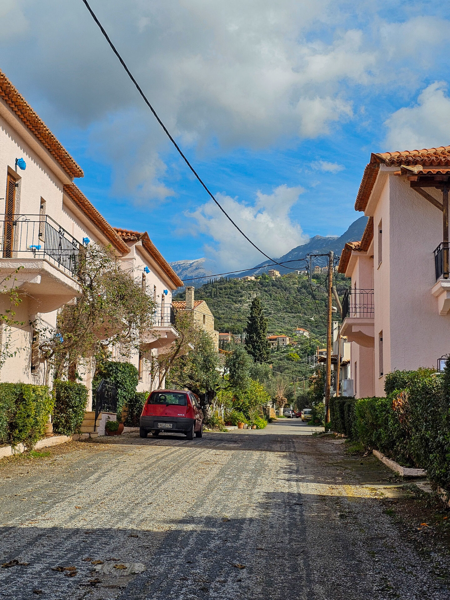 Quiet residential street in Kardamili, Greece with mountain views and traditional Mediterranean houses.