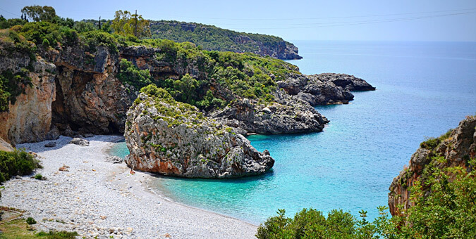 Scenic view of Foneas Beach near Kardamili, with turquoise waters, white pebbles, and dramatic rocky cliffs.