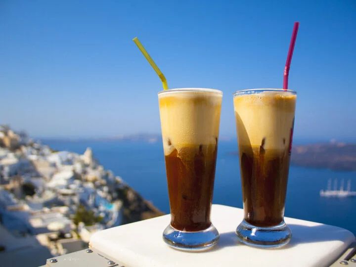 Two Greek frappé iced coffees with straws overlooking the Aegean Sea