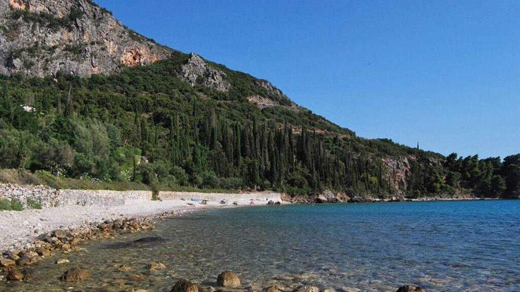 Kalamitsi Beach in Kardamili, with crystal-clear water and a lush cypress-covered hillside