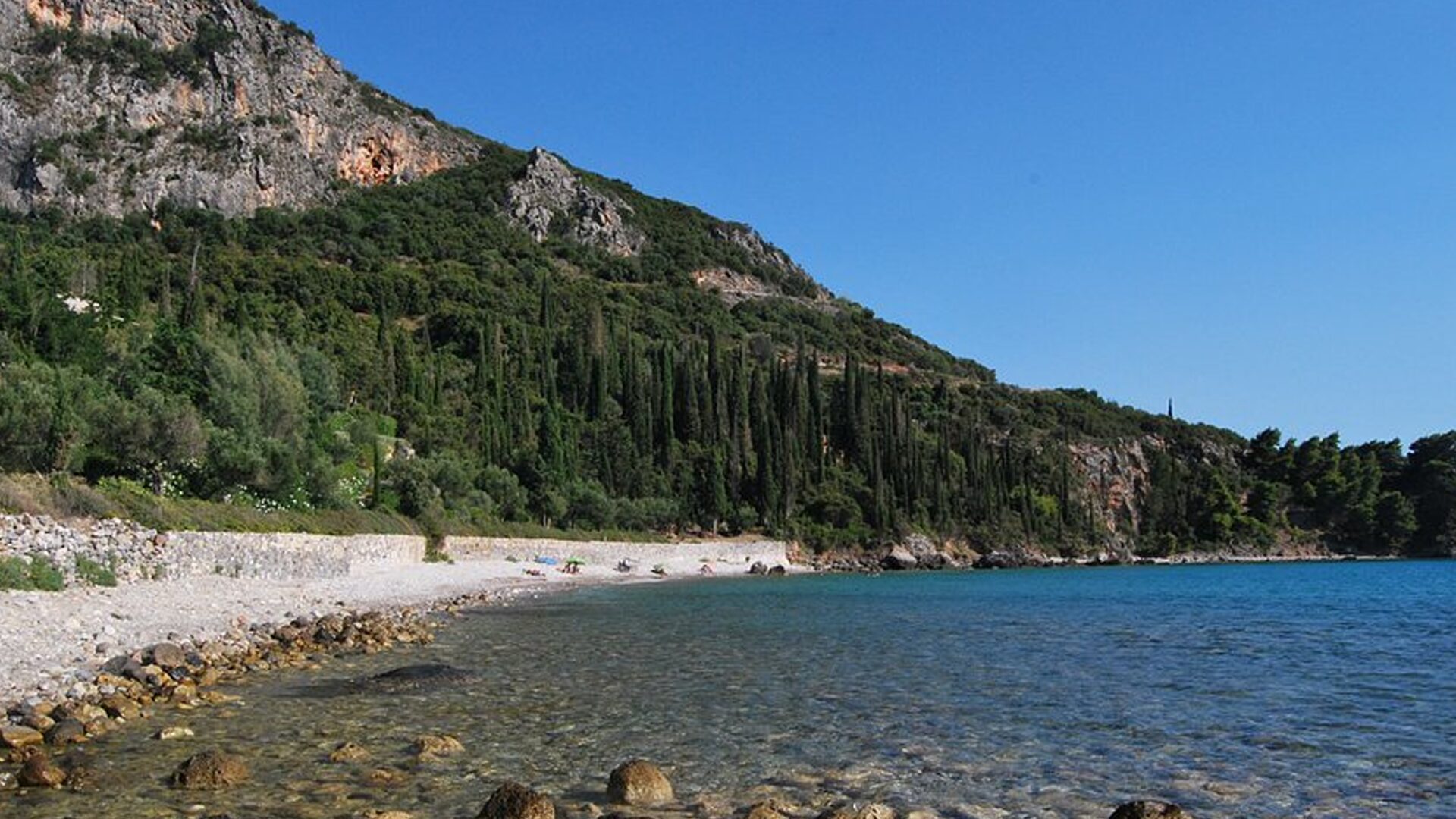 Kalamitsi Beach in Kardamili, with crystal-clear water and a lush cypress-covered hillside