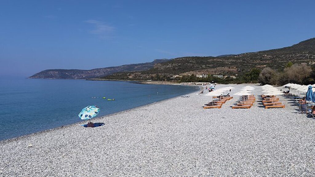 Ritsa Beach in Kardamili with sunbeds, umbrellas, calm blue water, and a scenic mountain backdrop on a clear summer day