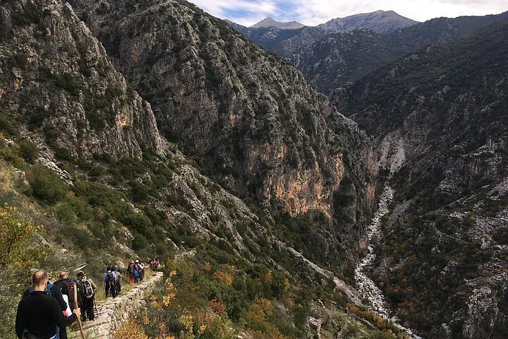 Hikers walking along the rugged Viros Gorge trail near Kardamili, surrounded by dramatic cliffs and lush greenery.