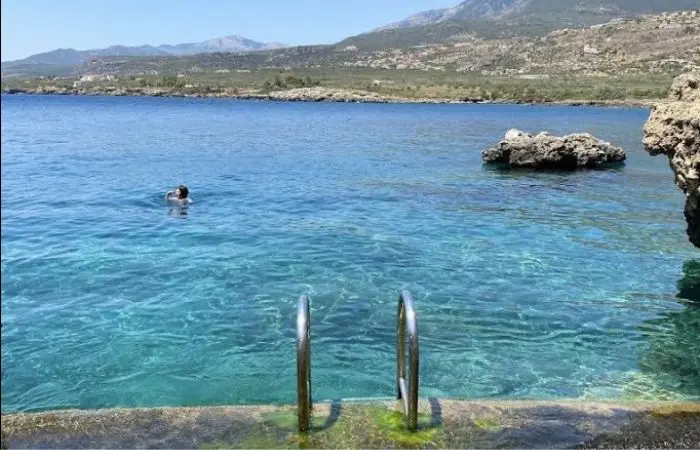 Swimmer enjoying clear turquoise water at Gnospi Beach cove in Mani, Greece with Taygetus mountains in the background