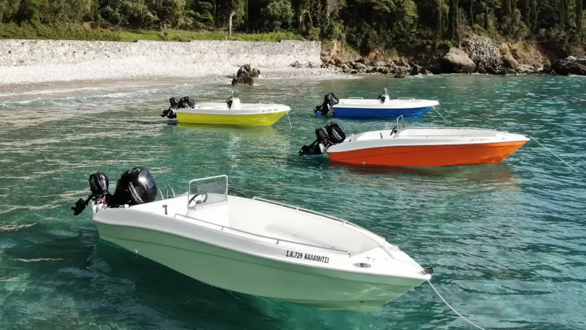 Small colorful boats anchored near a pebbled shore in Kardamili, Greece, available for rental to explore the Mani coastline.