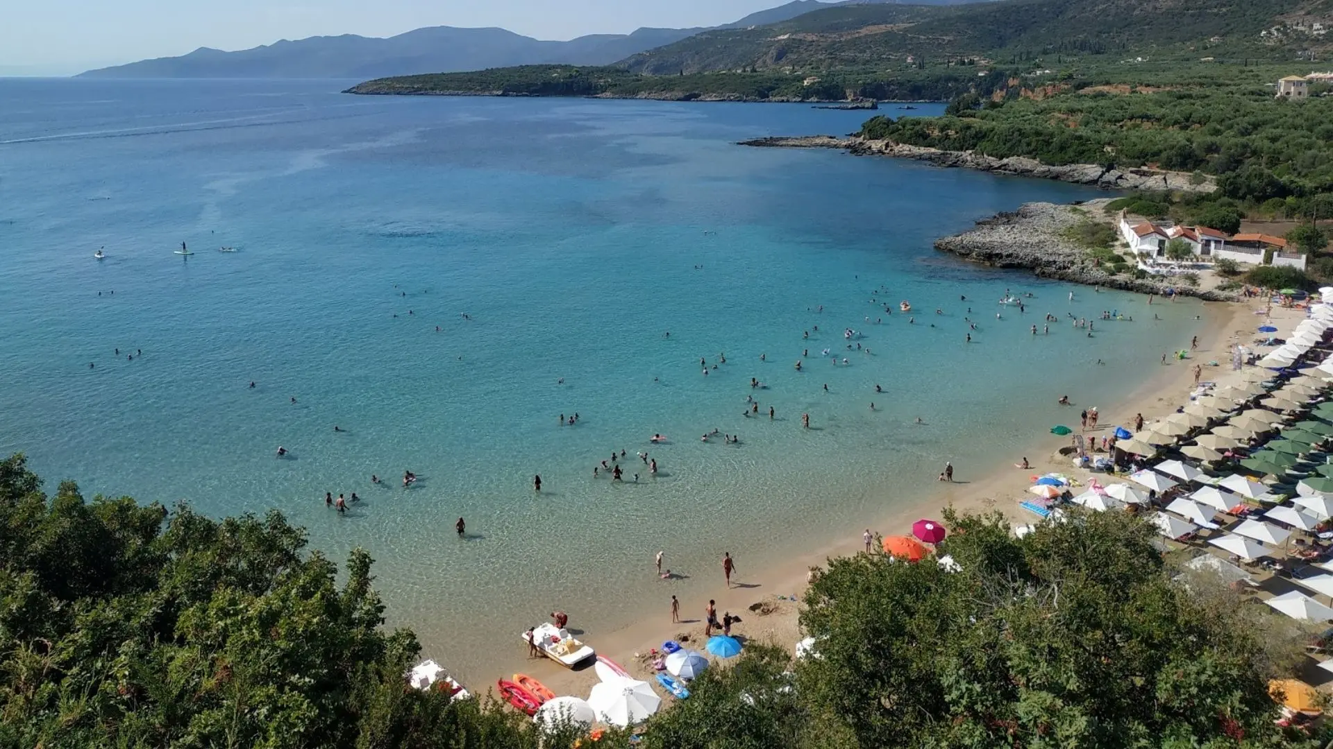 View of Paralia Kalogrias Beach in Stoupa, Mani, Greece with clear turquoise waters, sunbeds, and swimmers