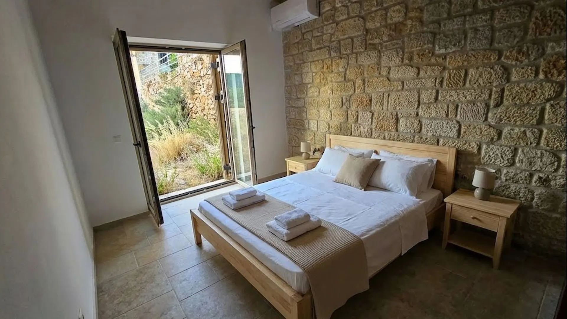 Luxurious boutique hotels bedroom featuring a rustic Mediterranean stone accent wall, a professionally staged bed with crisp white linens, and warm ambient lighting.